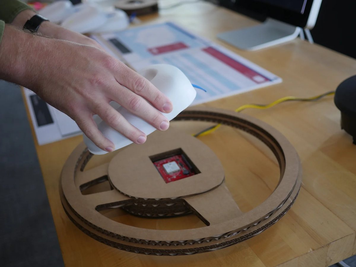 A hand placing a white airbag module onto a scanner set into a cardboard steering wheel.