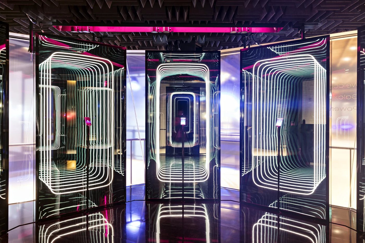 The installation on the event floor, with magenta light above and the mirrored columns running back into the room.
