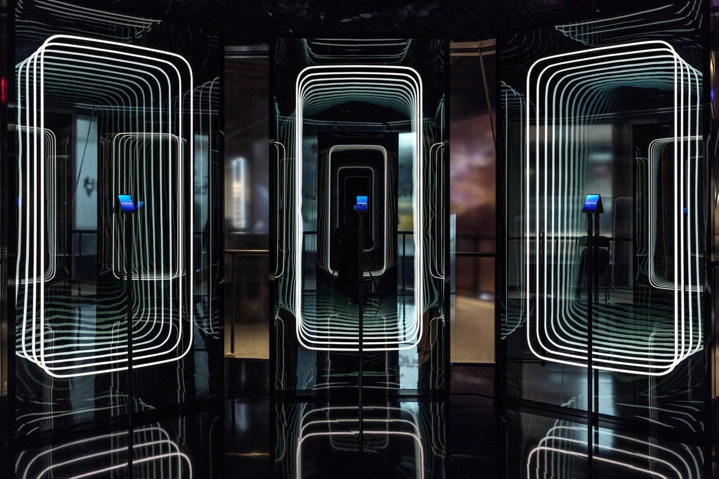 A row of tall infinity-mirror columns, each framing a phone in nested glowing outlines that appear to recede forever.