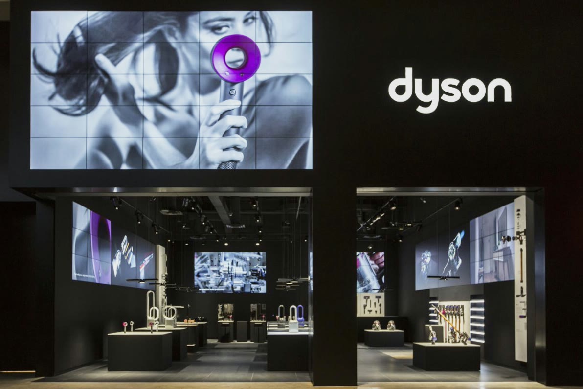 A Dyson boutique at night: a dark storefront with a large screen above the entrance and product displays inside.